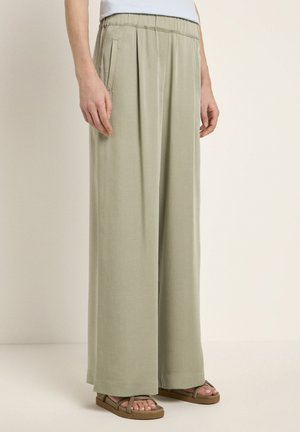 Light green wide-leg trousers with a pleated front, elastic waistband, and side pockets, paired with brown strappy sandals.