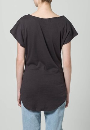 Czarny bawełniany t-shirt z szerokim dekoltem, krótkim rękawem i zaokrąglonym dołem, w połączeniu z jasnoniebieskimi dżinsami.