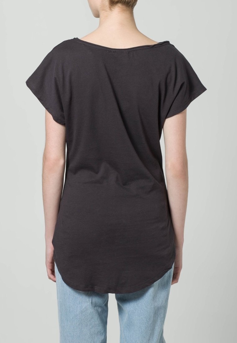 Camiseta de algodón negra con escote ancho, mangas cortas y dobladillo curvado, combinada con jeans de mezclilla azul claro.
