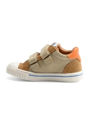 Beige en bruine suède peutersneaker met twee klittenbandsluitingen, witte rubberen neuskap en oranje hieltab met logo.