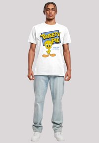 Hvit bomull t-skjorte med en fargerik "Tweety Pie" grafikk, med blå bakgrunn, iført lyseblå denim jeans og hvite joggesko.