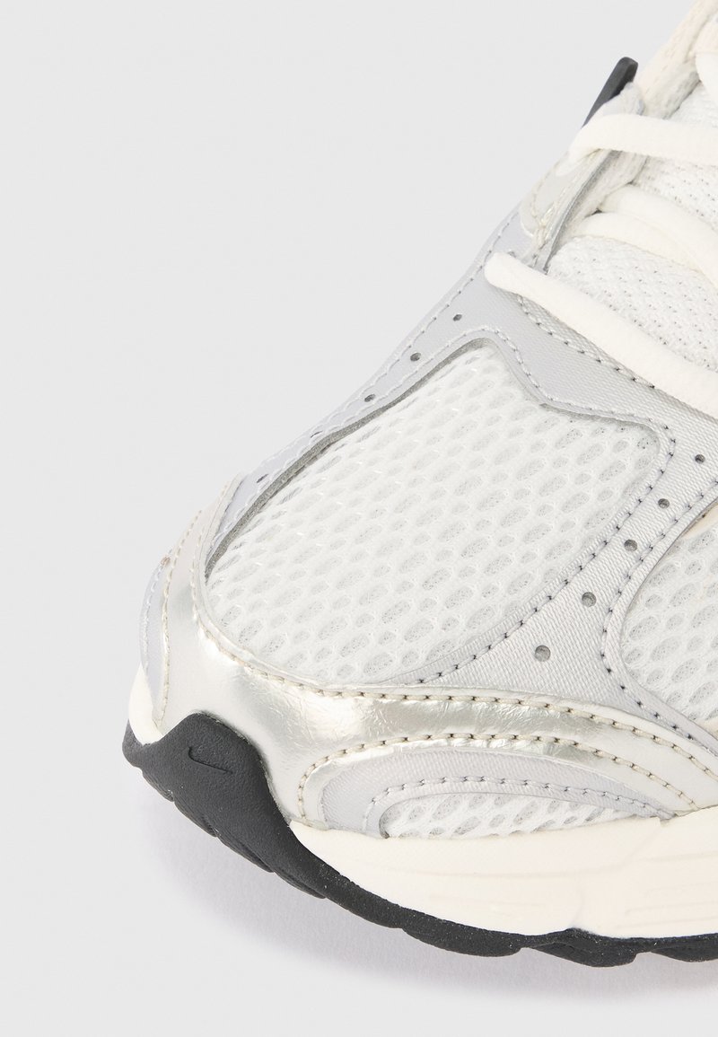 White and silver sneaker toe with mesh fabric, stitched overlays, white laces, and black textured sole.