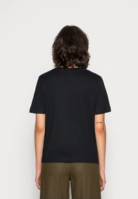 Svart bomullströja med korta ärmar och rund halsringning, med en enkel design. Baksidan har en liten textdetalj på den övre vänstra sidan.