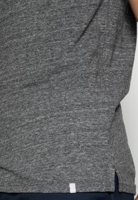 Grijze korte mouw t-shirt met een gestructureerde stof, afgeronde zoom en zijsplitten. Een klein wit label is zichtbaar aan de onderkant links.