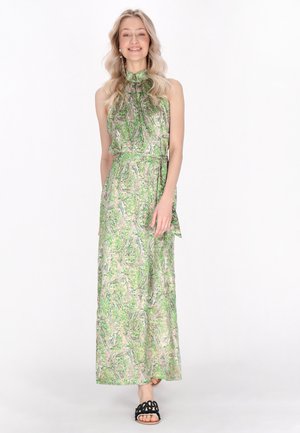 Abito maxi in fantasia paisley verde, tessuto setoso, scollatura alta, vita con cintura e lunghezza alla caviglia. Indossato con sandali neri con cinturini.