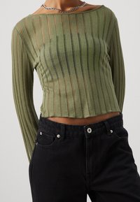 Olivgrünes, geripptes Langarmoberteil mit lässiger Passform, das vertikale Streifen aufweist und mit hoch taillierten schwarzen Jeans kombiniert wird.