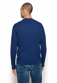 Kék kötött pulóver kerek nyakkal és hosszú ujjakkal, bordás mandzsettákkal és alján. Az anyag textúrája lágy és kényelmes.