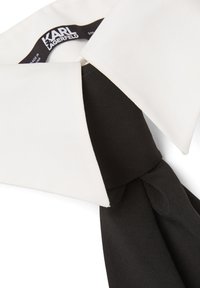 Cuello blanco y negro con una corbata negra. El cuello tiene una textura suave, mientras que la corbata parece ligeramente arrugada y texturizada.
