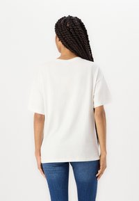 Vit bomull T-shirt med avslappnad passform, korta ärmar och rundad halsringning, uppvisad mot en neutral bakgrund.