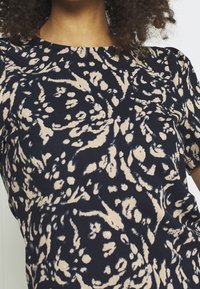 Navy blue patterned top with beige floral and abstract designs, round neckline, short sleeves, and smooth texture.