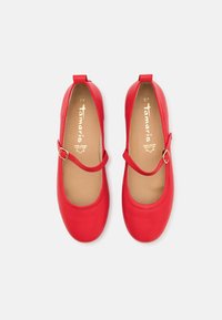 Une paire de chaussures Mary Jane en cuir rouge avec des sangles à boucle, des semelles intérieures beiges et des orteils ronds sur un fond blanc.