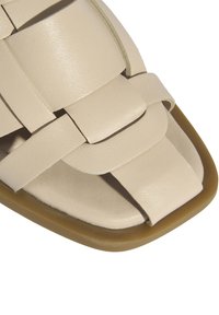 Sandale en cuir tressé beige avec une finition lisse, présentant un bout carré et une semelle en caoutchouc souple et arrondie.