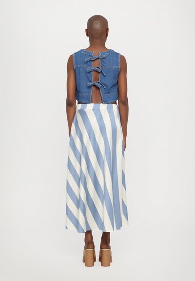 Denim crop top s triom mašnom na leđima, uparen s dugom suknjom s plavim i bijelim dijagonalnim prugama.