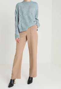 Jasnoniebieski sweter z dzianiny z ażurowym wzorem, zestawiony z beżowymi spodniami o szerokich nogawkach i czarnymi botkami na słupku.