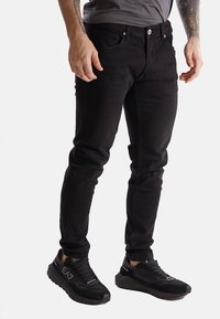 Jeans in denim neri con una vestibilità aderente, cinque tasche e chiusura con bottone. Abbinati a sneaker atletiche nere con una superficie texturizzata.