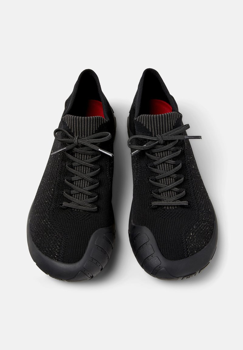 Svarta sportskor med ett texturerat stickat överdel och gummisålar, med snörning och en röd innersula.