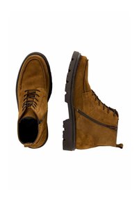 Braune Wildleder-Stiefeletten mit schwarzen Sohlen, seitlichen Reißverschlüssen und vorderen Schnürsenkeln, aus der oberen und seitlichen Ansicht auf weißem Hintergrund gezeigt.