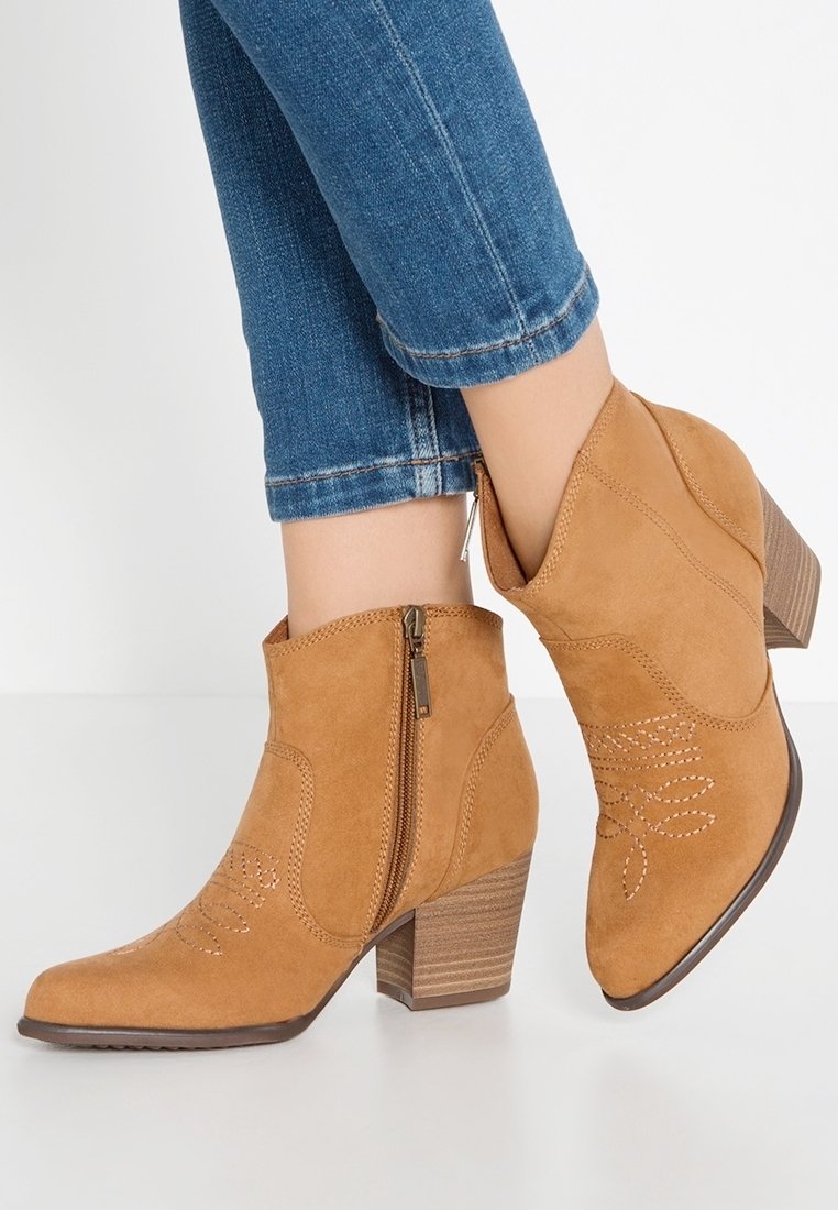 Bottes basses en daim couleur camel avec fermetures éclair latérales et petits talons empilés, portées avec un jean denim bleu.