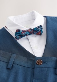 White dress shirt with blue floral bow tie paired with blue suit vest and matching pants featuring a brown button.