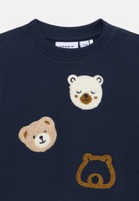 Marinblå sweatshirt med tre broderade björnhuvuden i beige och brunt. Ribbad yta med rund halsringning. Designad för spädbarn.