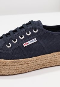 Námořnické plátěné tenisky s jute rope platformou, stříbrnými očky a bílou etiketou s logem "Superga". Klasický design s naučeným šněrováním.