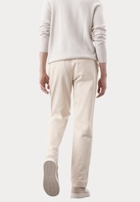 Off-white katoenen broek met een rechte broekspijp, gecombineerd met lichtbeige sneakers. Subtiele textuur, geen zichtbare patronen of hardware.