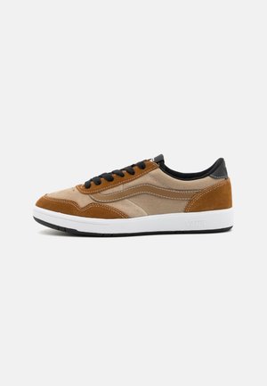 Zapatillas de deporte de ante y lona en tonos marrón y beige con cordones negros, entresuela blanca y suela de goma negra. Presenta rayas laterales en contraste.