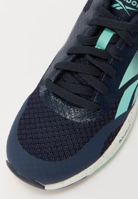 Baskets de sport navy avec tige en mesh, accents texturés et détails turquoise. Équipées de lacets noirs et d'une semelle intermédiaire blanche mouchetée.