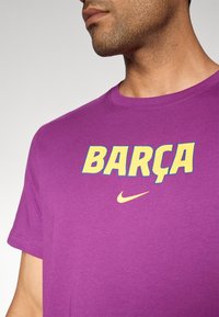 Lilla bomulds t-shirt med "BARÇA" i gul og blå tekst, med et lille gult Nike-logo nedenfor. Korte ærmer og rund halsudskæring.