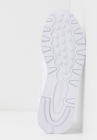 Semelle blanche de basket Reebok avec grip texturé, picots circulaires et logo embossé au centre.