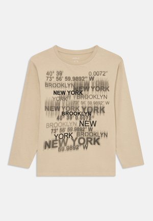 Beige Langarm-T-Shirt mit schwarzem Aufdruck von Städtenamen und geografischen Koordinaten in verschiedenen Schriftarten und -größen.