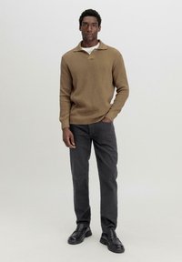 Brauner gestrickter Pullover mit Kragen, kombiniert mit dunkelgrauen, gerade geschnittenen Hosen und schwarzen Slippern. Minimalistisches Design.
