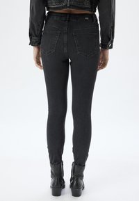 Jeans ajustados de cintura alta negros con una textura suave, diseño de cinco bolsillos y sutilezas en las costuras en la parte trasera, combinados con botines negros.