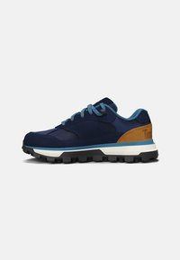 Zapatillas deportivas marinas con cordones azules, que presentan una parte superior oscura con textura y un acento de cuero marrón, complementadas por una suela negra resistente.
