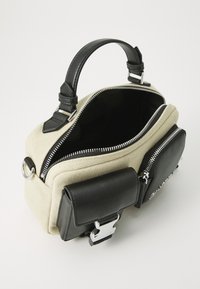 Canvas and leather handbag with a black handle, silver zippers, and a front pocket. Features a cream body and black accents.
