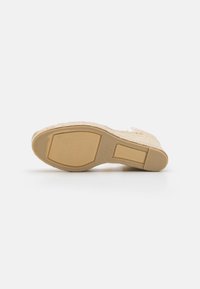 Espadriglia intrecciata beige con tomaia texturizzata, dettagli simili a juta, suola in gomma liscia color tan e branding sottile sulla parte inferiore.