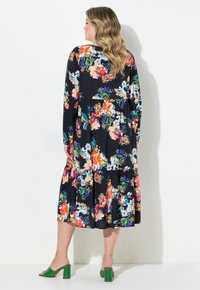 Blommig maxiklänning med långa ärmar, svart bas, livfulla orange, rosa och gröna mönster, volangdesign, tillsammans med gröna blockklack-sandaler.