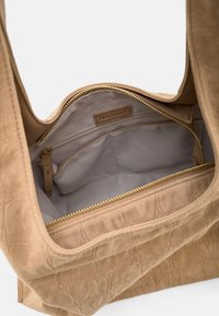 Beigefarbene Wildleder-Shopper-Tasche mit strukturiertem Äußeren, ausgestattet mit einem mit Stoff ausgekleideten Innenraum, Reißverschlusstasche und Logoplakette. Goldfarbene Metallakzente.