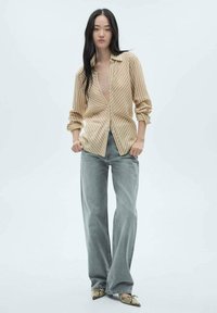 Camicia a righe beige e bianche con bottoni, pantaloni larghi in denim grigio e scarpe a punta con motivo rettile. Tessuto morbido e vestibilità casual.