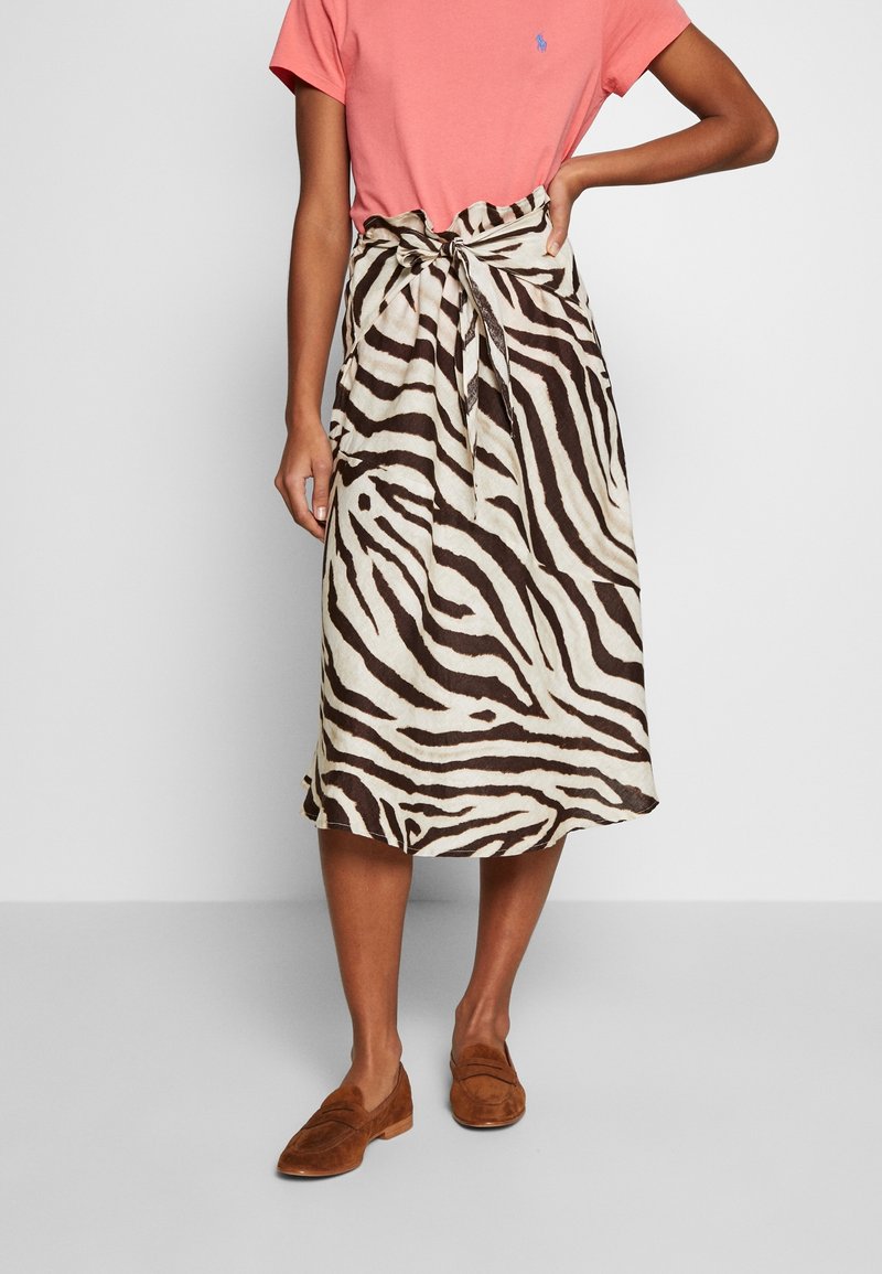 Zebra-patterned midi skirt in beige and dark brown, made of lightweight fabric, featuring a tied waist and a relaxed fit. Paired with a pink shirt and brown loafers.