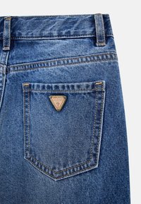 Jeans de mezclilla azul con un parche de cuero triangular en el bolsillo trasero, con costuras en contraste y un diseño clásico de cinco bolsillos.