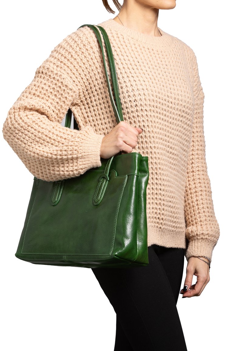 Borsa a tracolla verde in pelle con due manici superiori, forma rettangolare, superficie liscia e dettagli di cucitura sottili. Indossata con un maglione beige in maglia.