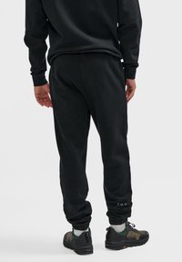 Schwarze Jogginghosen mit schmal zulaufenden Bündchen, elastischem Bund und sichtbaren Nähten. Auf der Rückseite ist "F.U.T." in der Nähe des Saums gestickt.