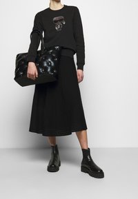 Svart sweatshirt med grafisk design, svart midkjol, quiltad svart tote-väska och kraftiga svarta ankelstövlar. Slät textur genomgående.