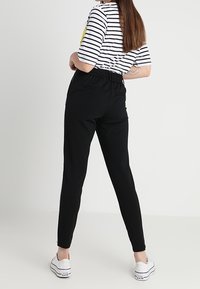 Sorte, elastiske joggers med tætsiddende ben, stylet med en kortærmet bluse med vandret strib og hvide canvas sneakers.