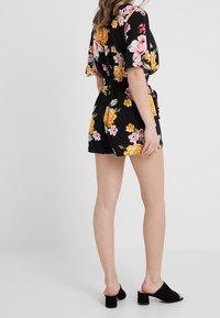 Musta kukkamekko, jossa on eläväinen sekoitus vaaleanpunaisia ja keltaisia kukkia, lyhythihaiset, joustava vyötärö ja sileä kangas. Yhdistetty mustiin muloihin.