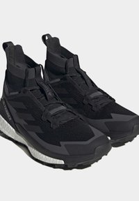 Schwarze Sportschuhe mit einem gestrickten Obermaterial, gepolstertem Schaft und strukturierten Details. Sie verfügen über eine weiße Zwischensohle und eine robuste schwarze Außensohle für besseren Halt.