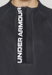 Top sportivo nero con scollo zip, texture a pois e audace logo "UNDER ARMOUR" lungo la zona della zip.