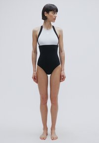 Μαύρο-άσπρο ολόσωμο μαγιό με ψηλή λαιμόκοψη, τιράντες τύπου racerback και εφαρμοστή σχεδίαση. Ομαλή υφή και μονόχρωμες επιφάνειες.