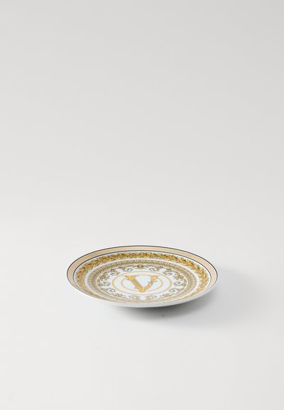 Balta porcelāna šķīvis ar zelta dekoratīvu malu, ziedu rakstiem un centrālo burtu "V" greznā dizainā.